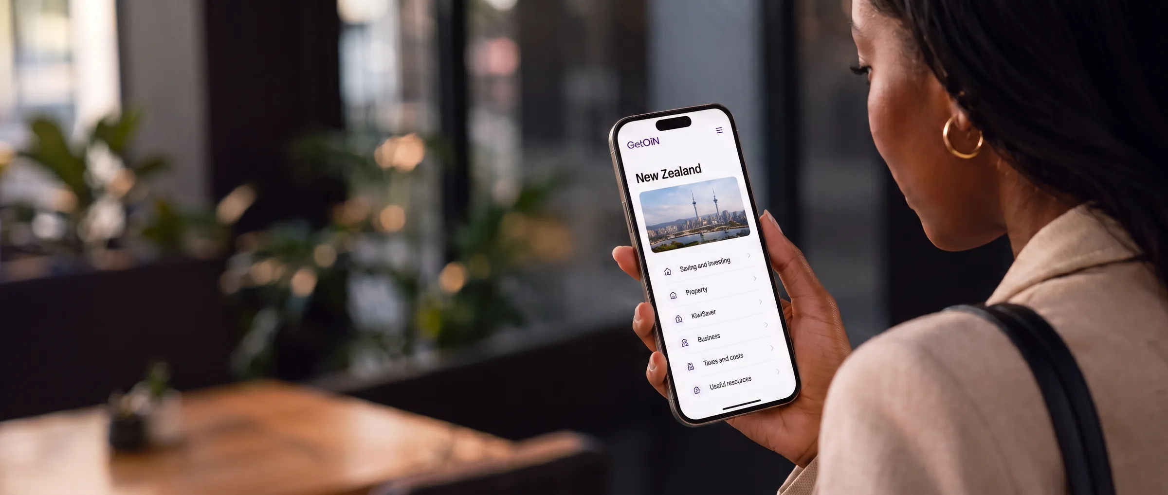 Woman holding a phone showing the GetOiN New Zealand country guide